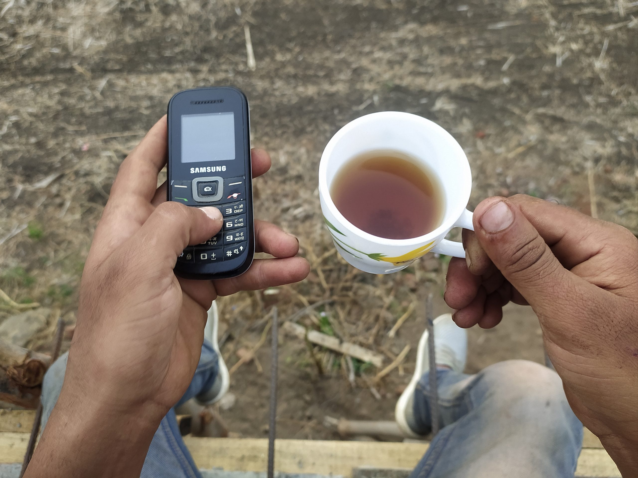 A keypad phone and tea cup in hands