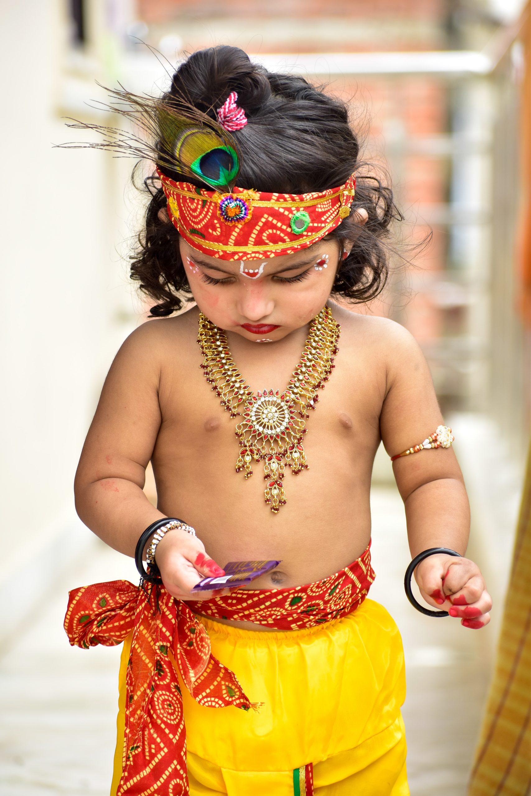 Baby dressed as Krishna holding chocolate